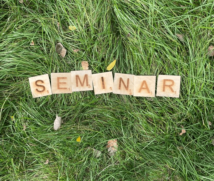Wooden scrabble tiles in a field spelling 'seminar'