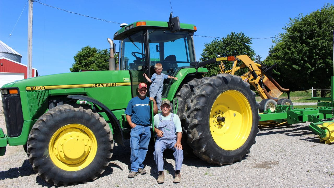 A family sitting on a tractor in front of a dairy farm