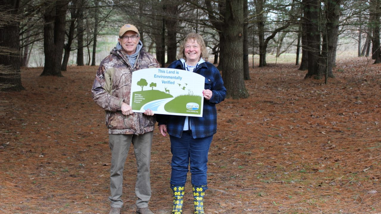 The Hansen couple, holding a verified sign in a pine forest