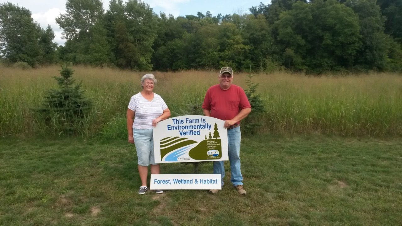 Miller couple standing with a sign indicating their forest, wetland and habitat is MAEAP verified