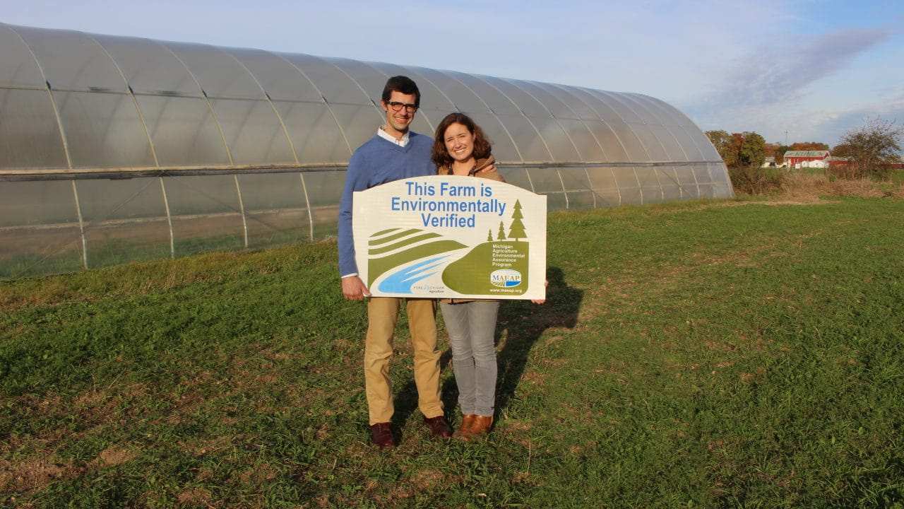 Two people standing with a MAEAP verified sign in front of a hot house
