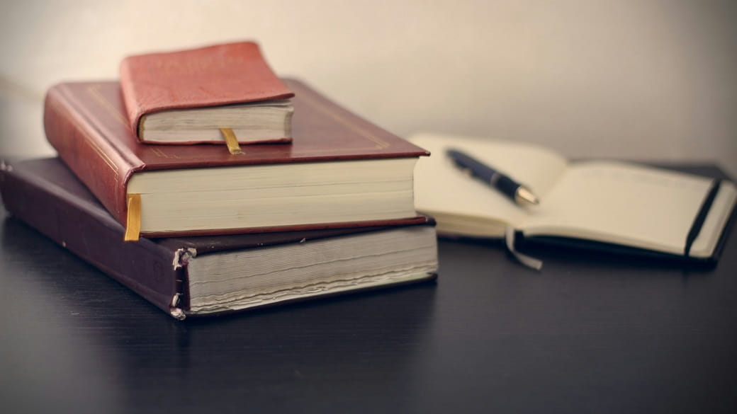 Several books, one open with a pen