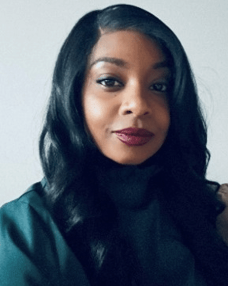Kenya Lowe: A headshot-style image of a black woman with long, dark wavy hair wearing a dark green top and burgundy lipstick. She is facing the camera with a slight smile and neutral background lighting.