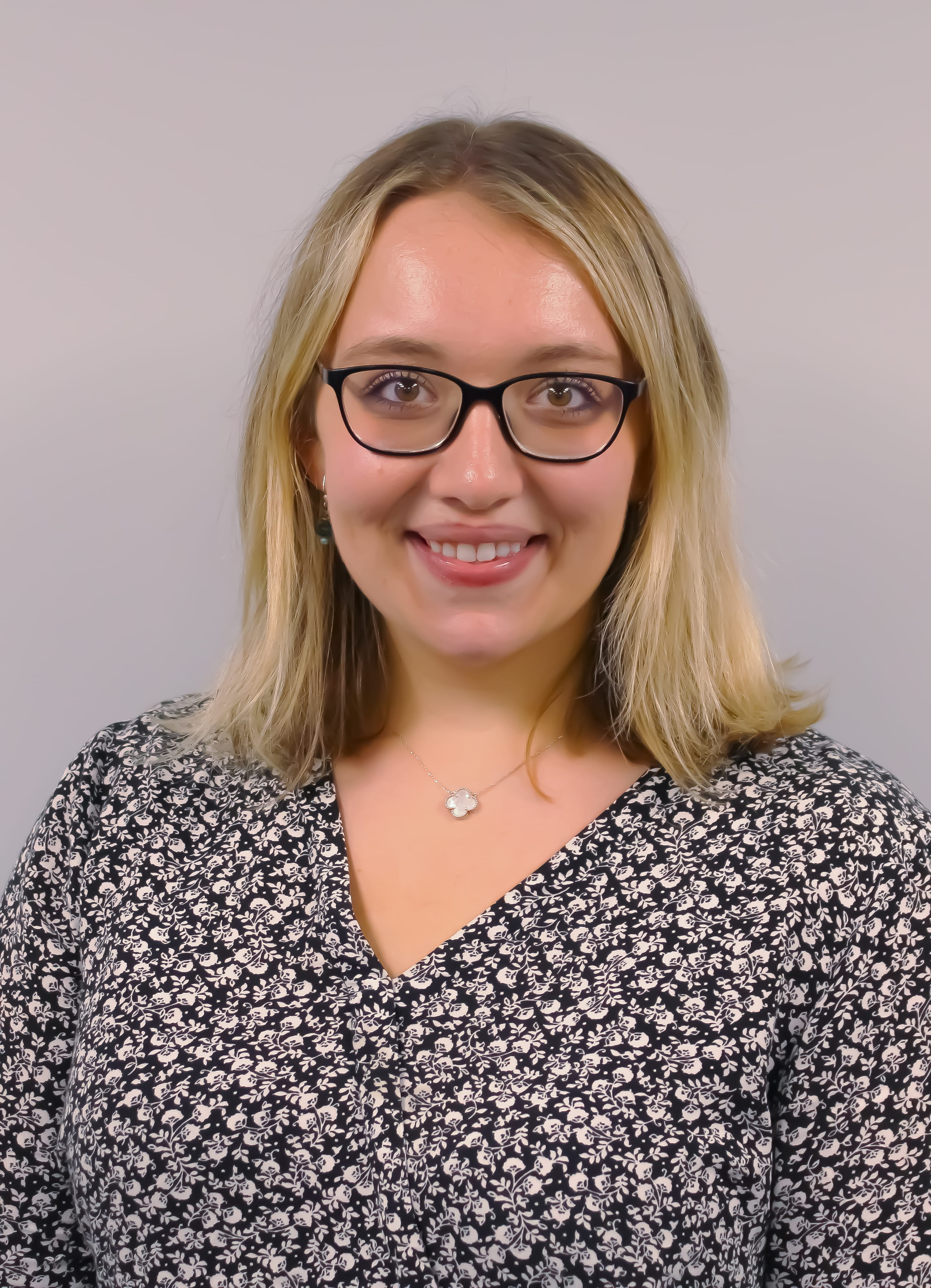 Image of a woman with shoulder length blonde hair, glasses, and a dark patterned shirt 