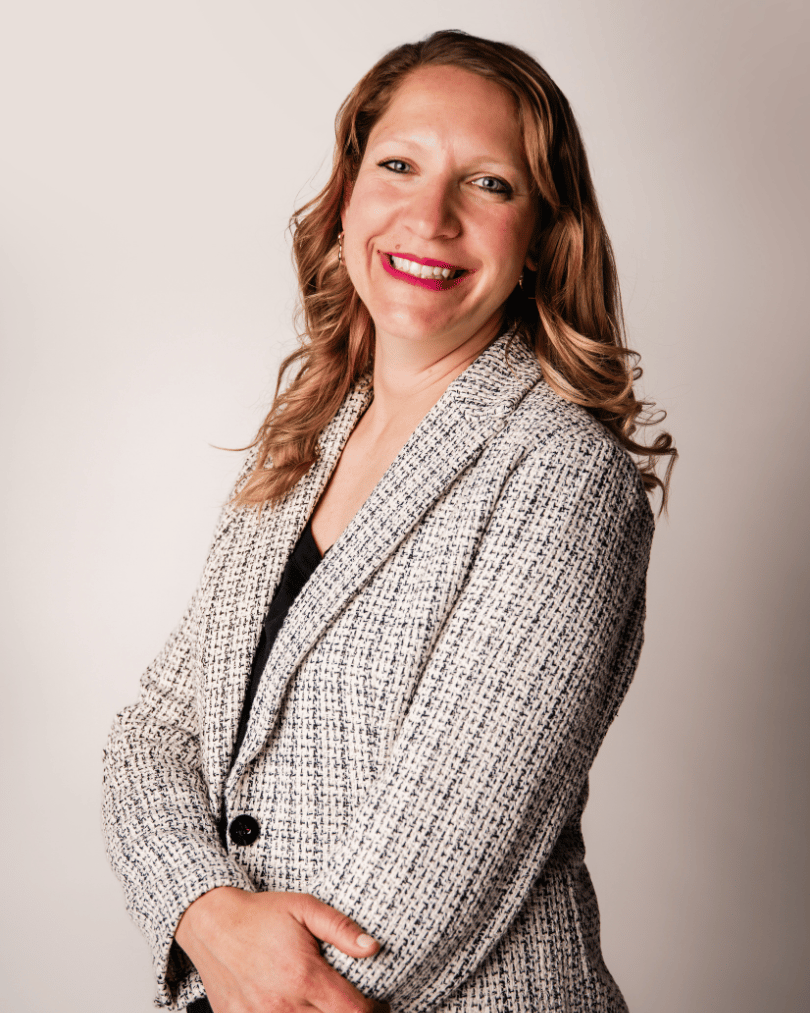 A photo of Joanne Forbes, a person with long, blonde hair wearing a light colored jacket, standing sideways against a light background