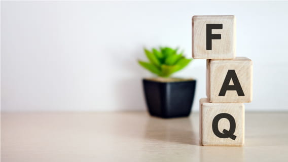 Wooden blocks stacked vertically spelling "FAQ" on light wooden desk with small succulent in background.