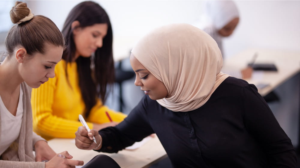 African American woman in hijab assisting female high school student.