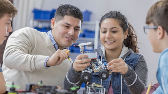 teacher and high school student working on robotics car while two other students watch