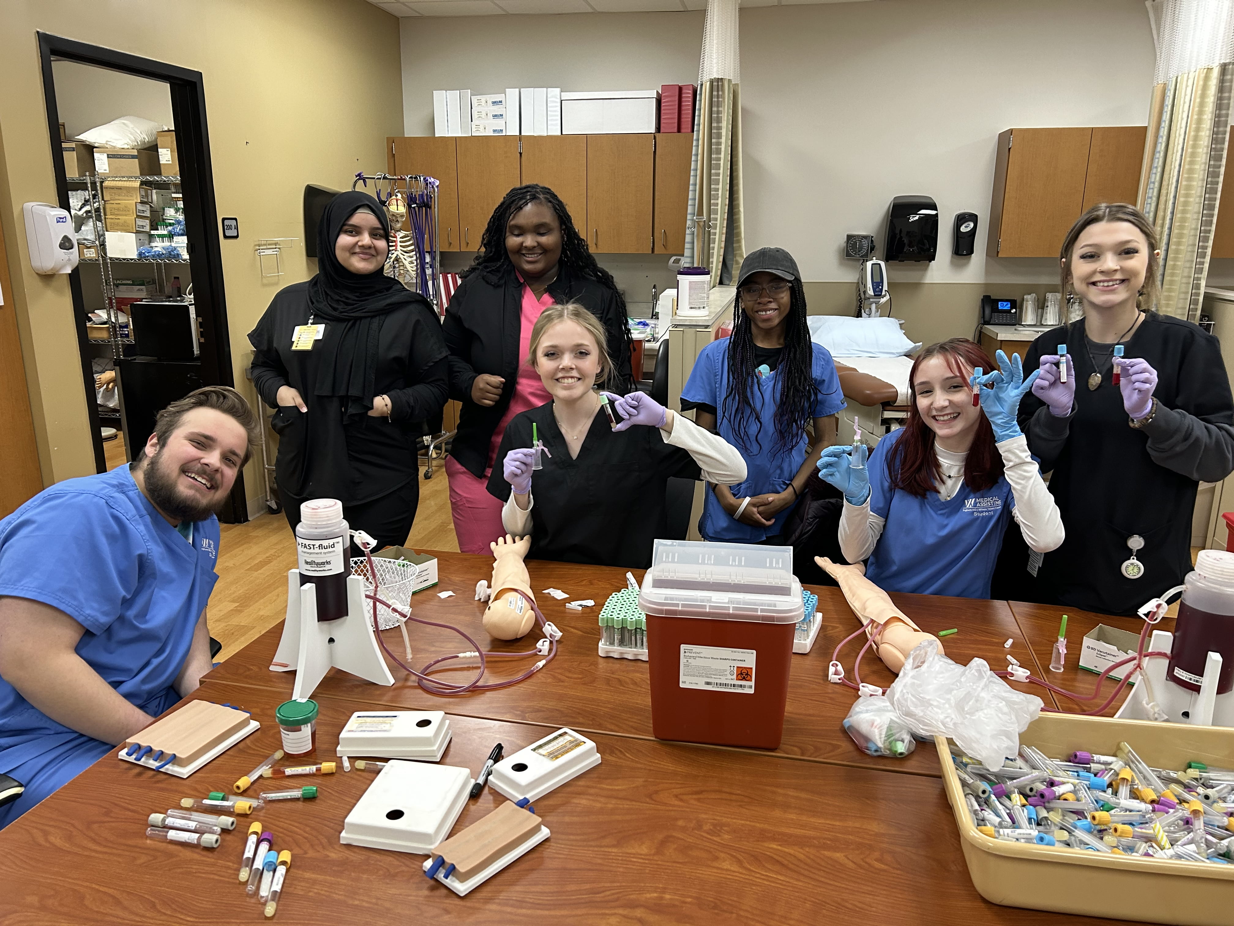 Healthcare students practicing on the trainer arms for phlebotomy.