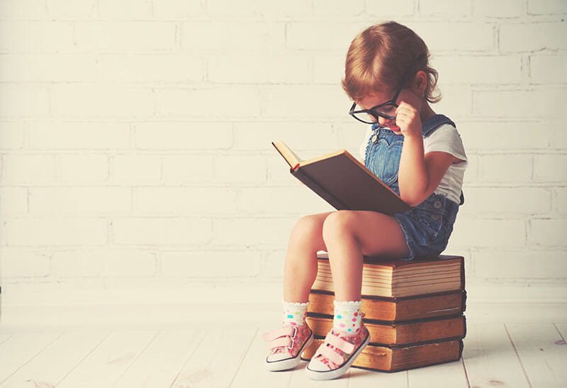 small child reading a book while sitting on top 3 books
