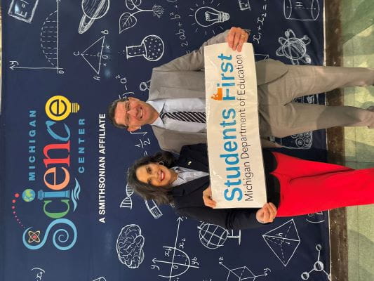 Left to right woman and man holding students first banner