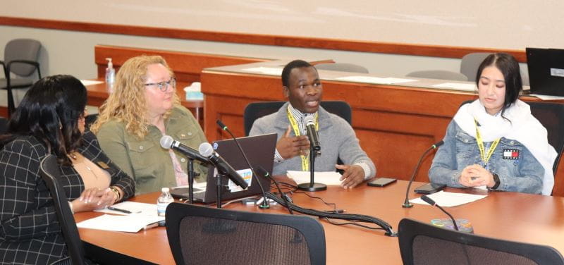 4 people sitting at end of board table presenting