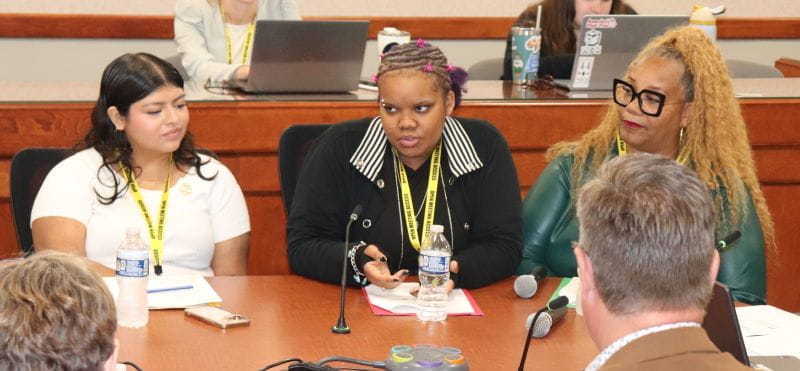 Three students presenting at a board table