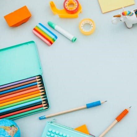Colored pencils, erasers, tape, and other office supplies on a light blue desk.