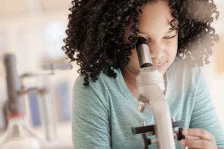 Close-up of girl in science classroom, looking through a microscope