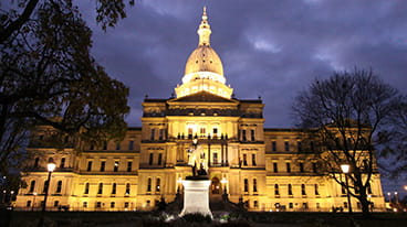 The front of the Michigan Capitol Building lit up at twilight