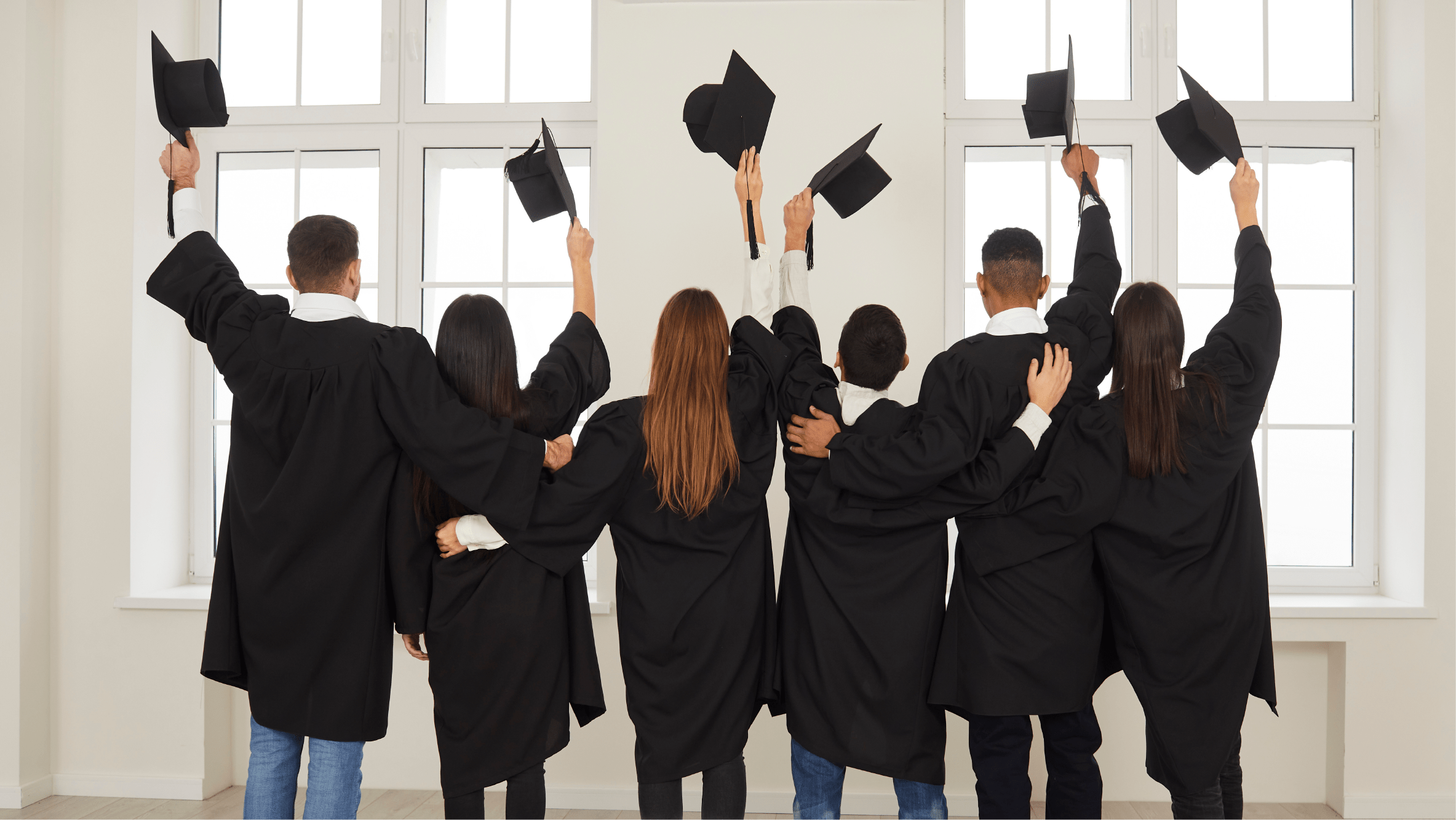 Group of diverse high school graduates in gowns with caps raised in the air walking away from camera.