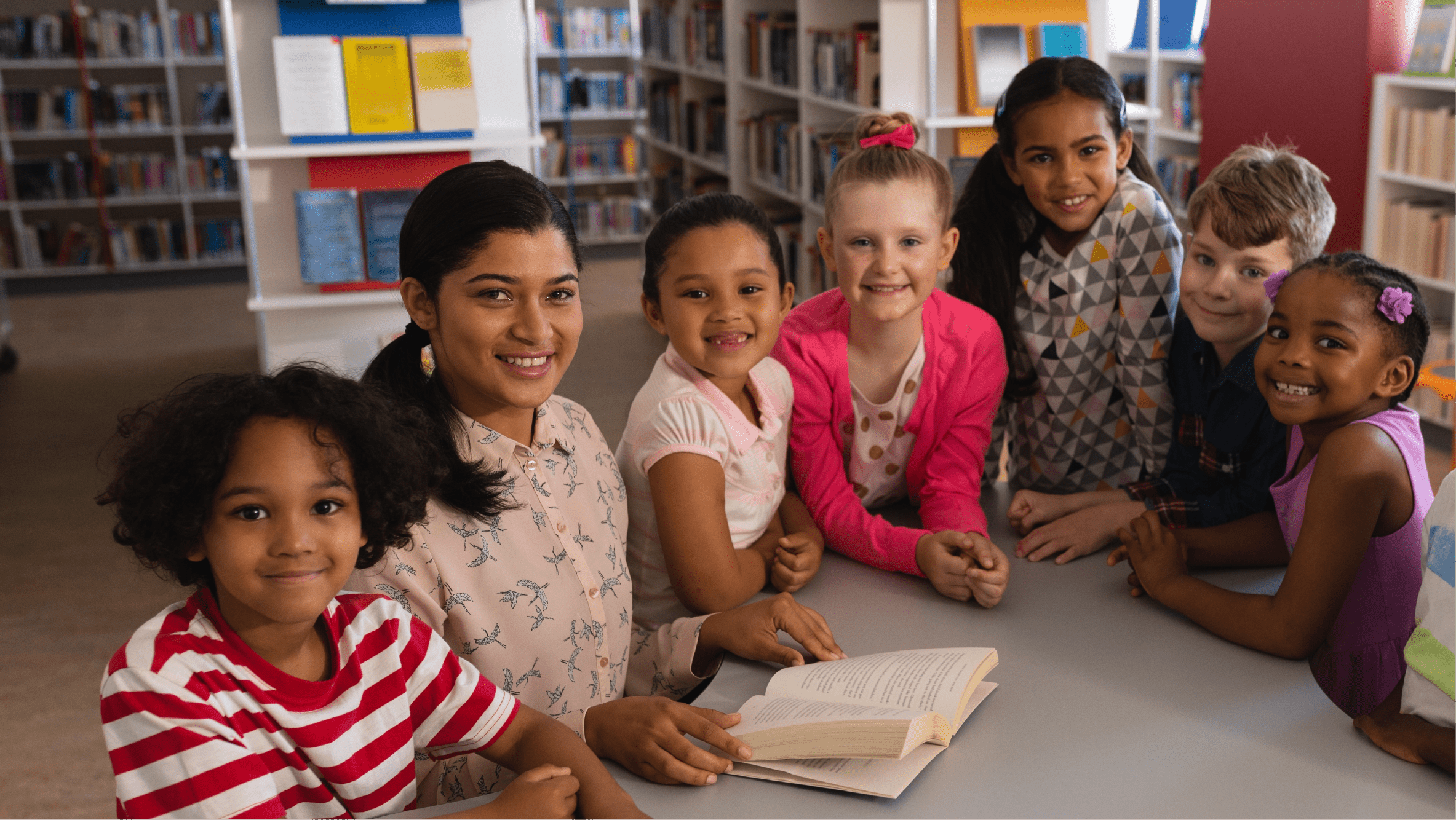 Diverse group of elementary students and teacher seated at table in library