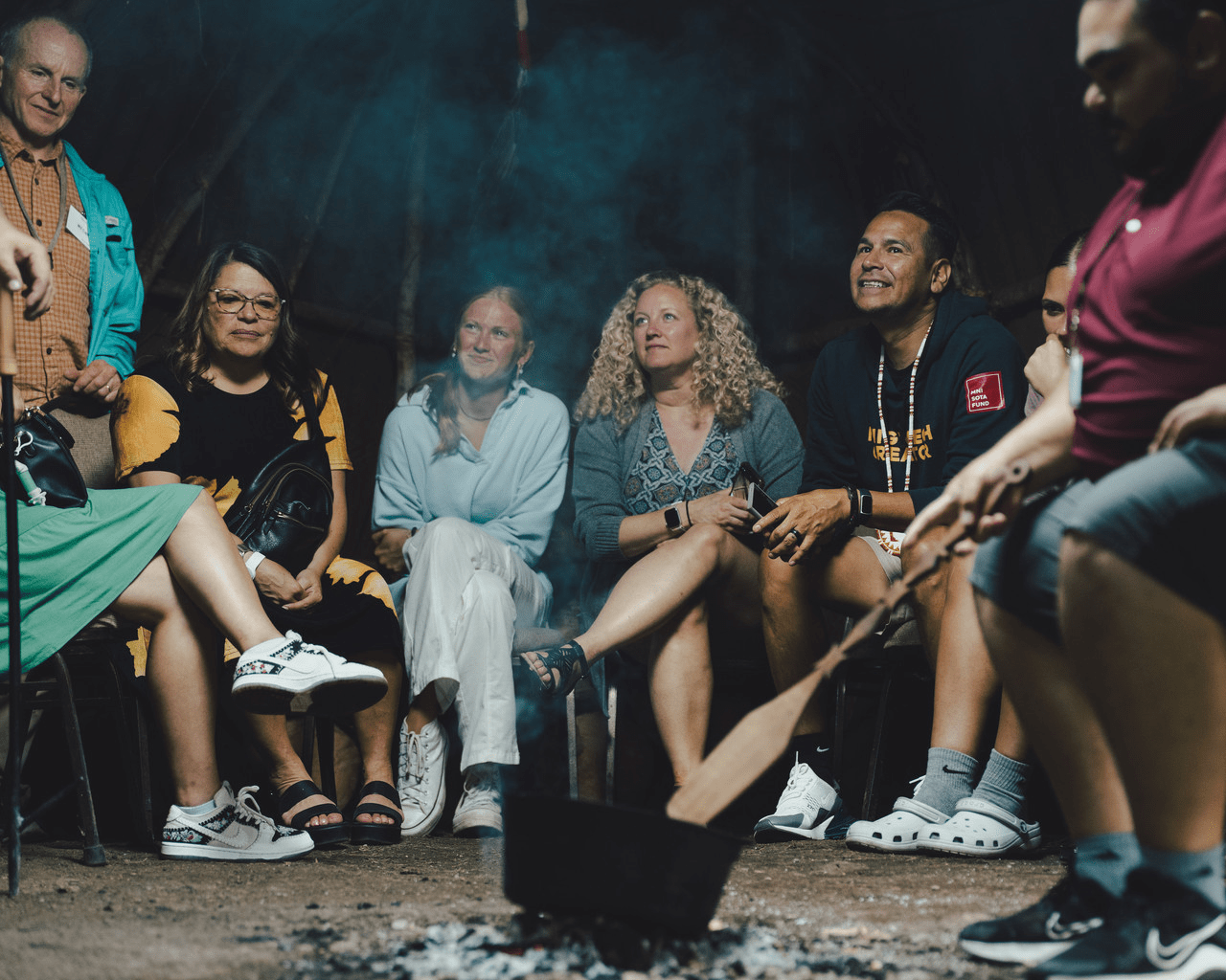 Diverse group of adults gathered around a fire sharing knowledge.