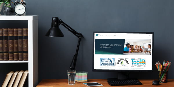 Desk with computer showing Michigan Department of Education home page on screen.