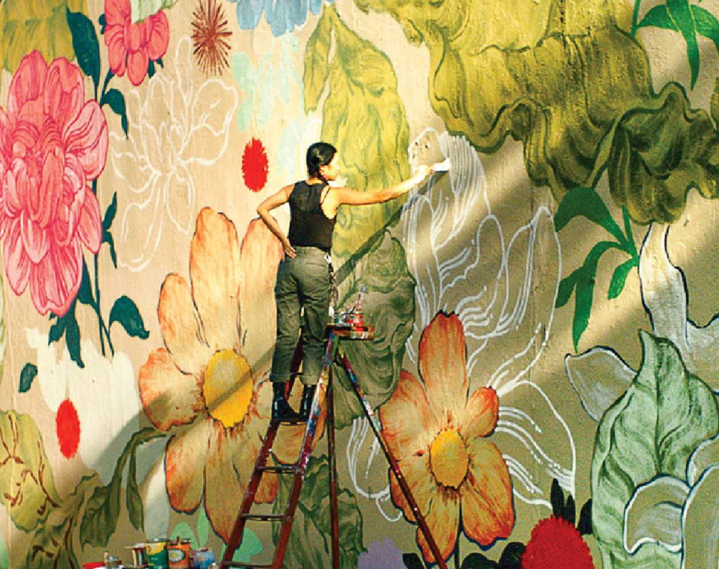 An artist stands on a ladder in front of a large floral mural