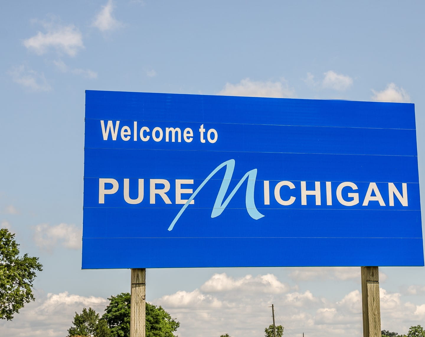 Blue sign along a roadway reads Welcome to Pure Michigan