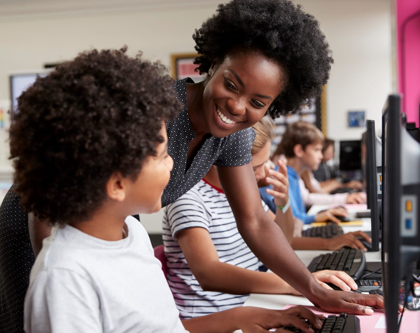 A female teacher helps a young boy use a computer