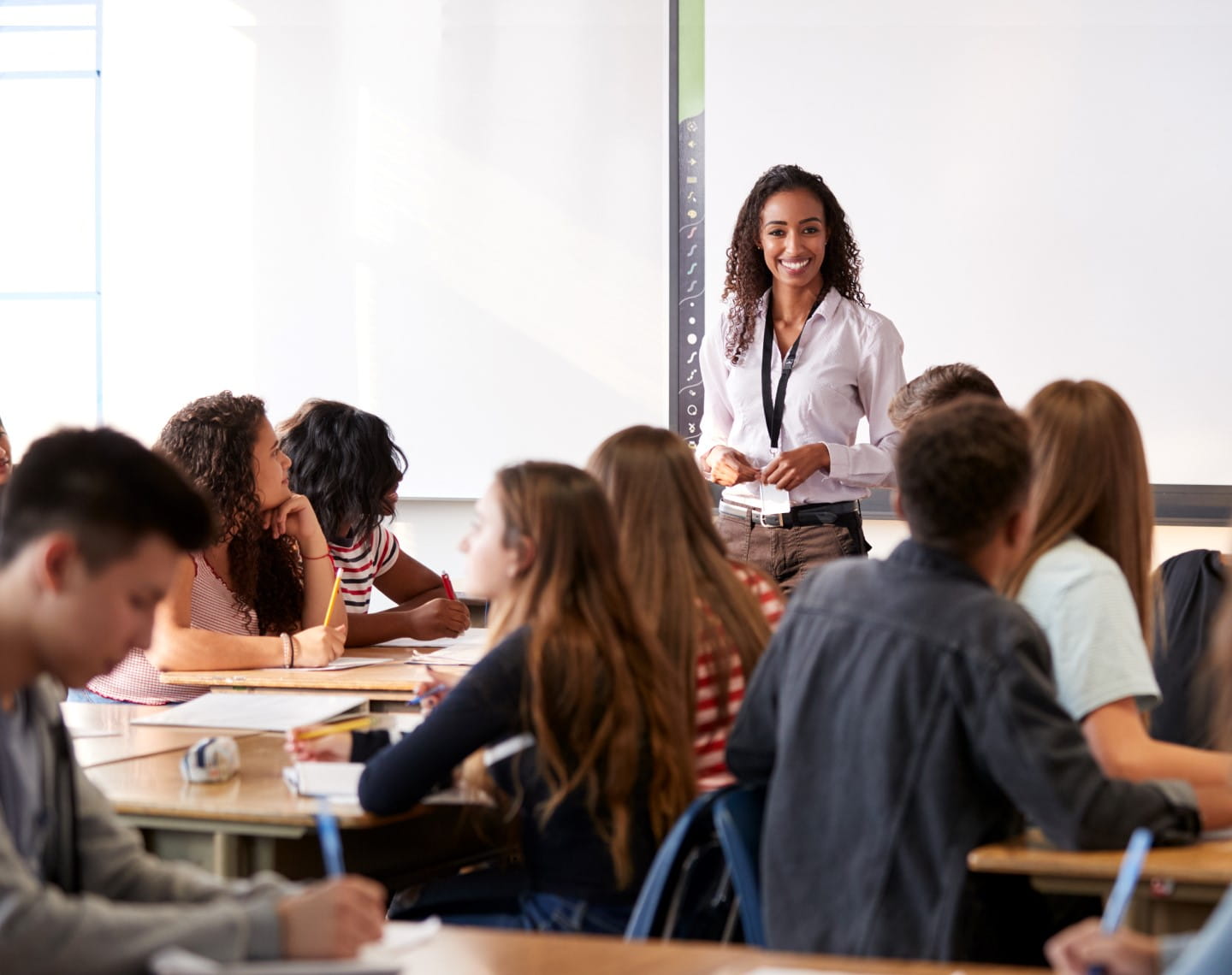 A female teacher stands in front of a classroom filled with teenage students