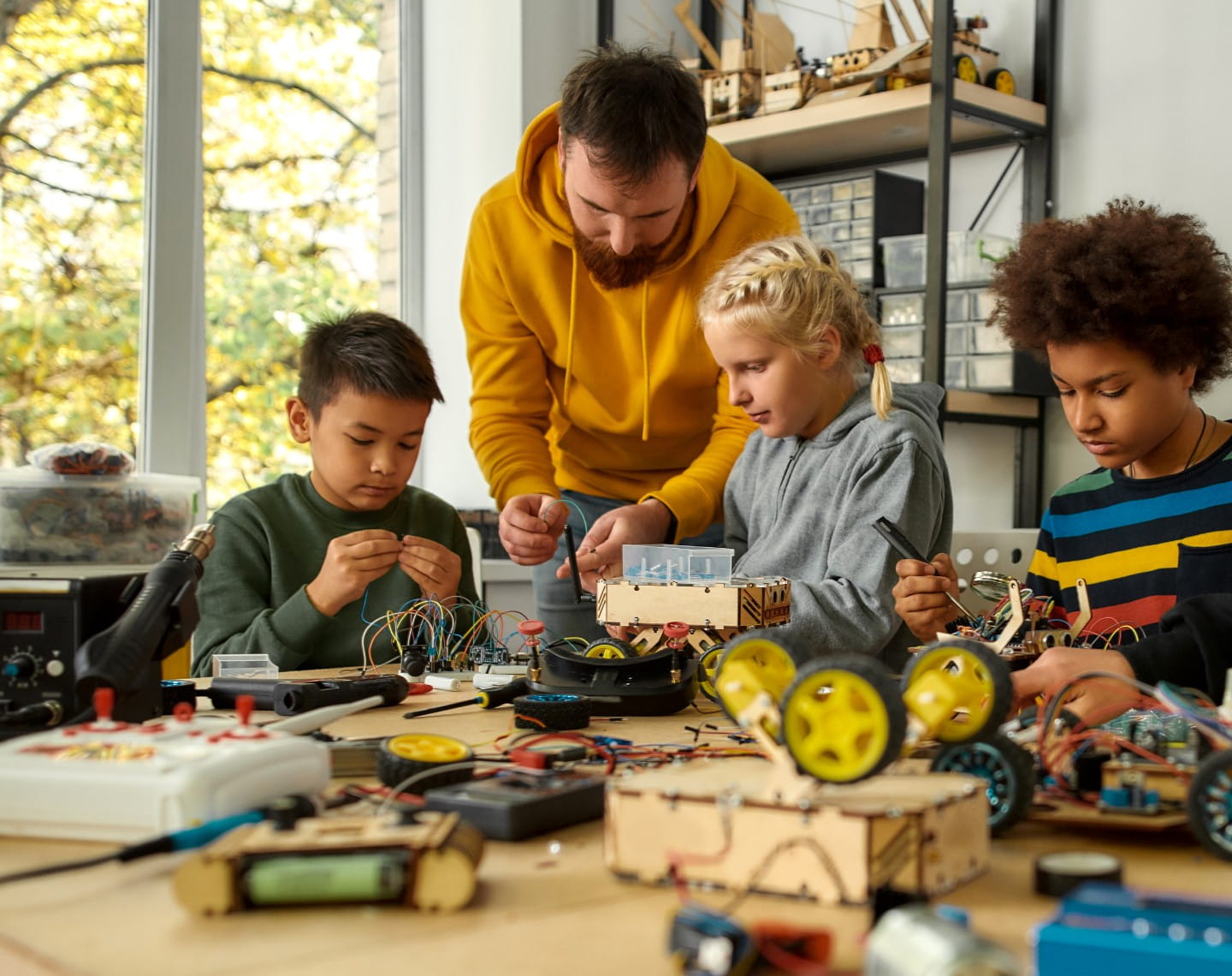 A male teacher works with a group of young students on a robotics project