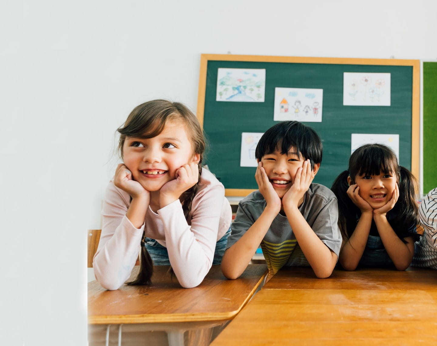 Three elementary students are resting their chins in their hands and smiling at the camera