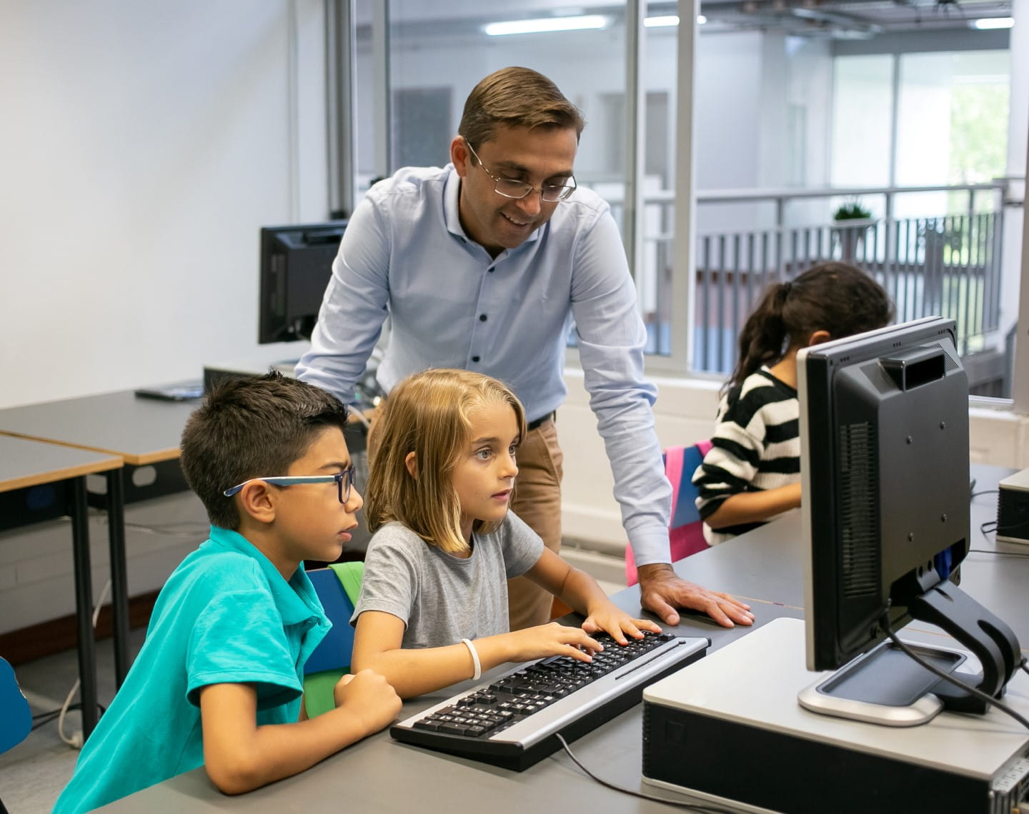 A male teacher works with two elementary students at a desktop computer