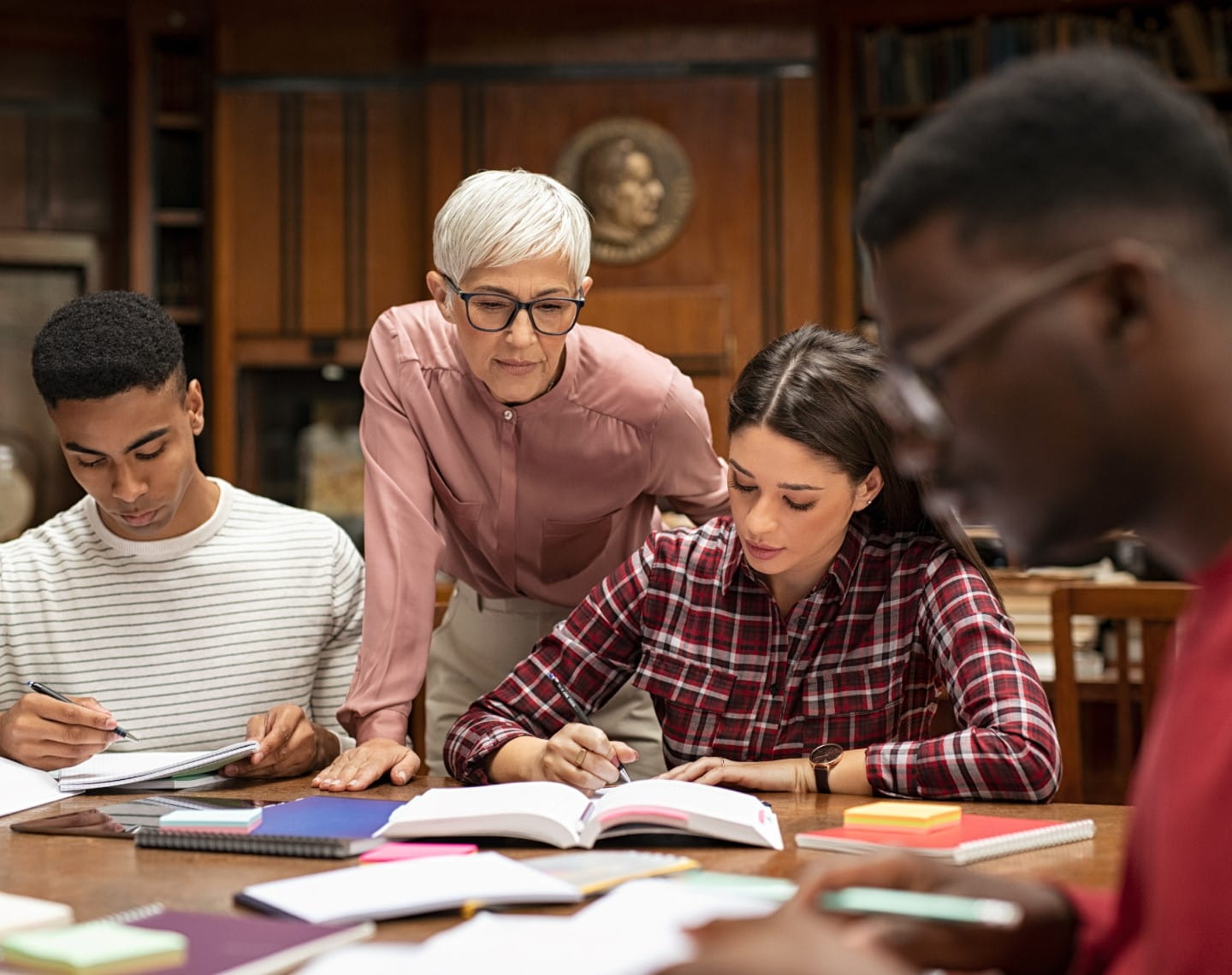 A female college professor wearing glasses works with a group of education students at a large table