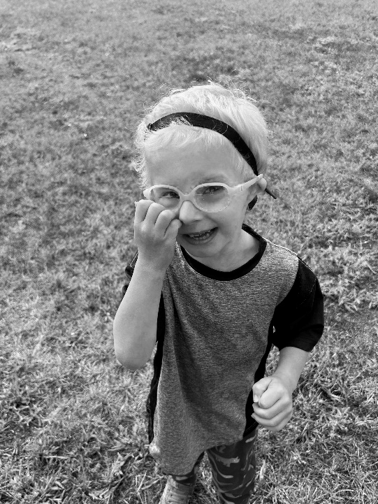 Ethan, a young boy wearing glasses, smiles up at the camera while standing outdoors.