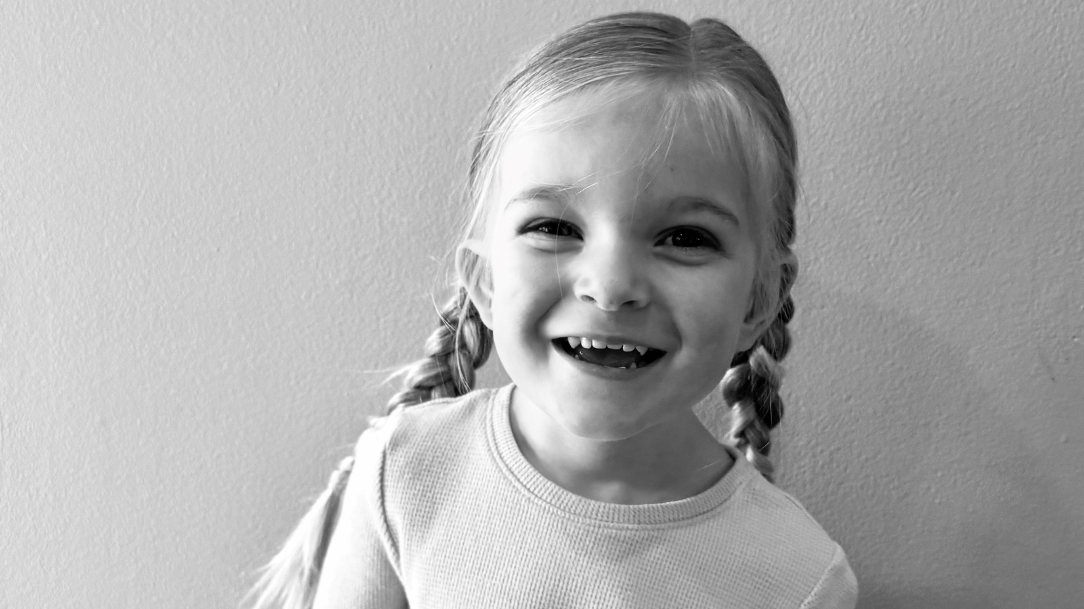 A young girl with braided pigtails smiles at the camera.