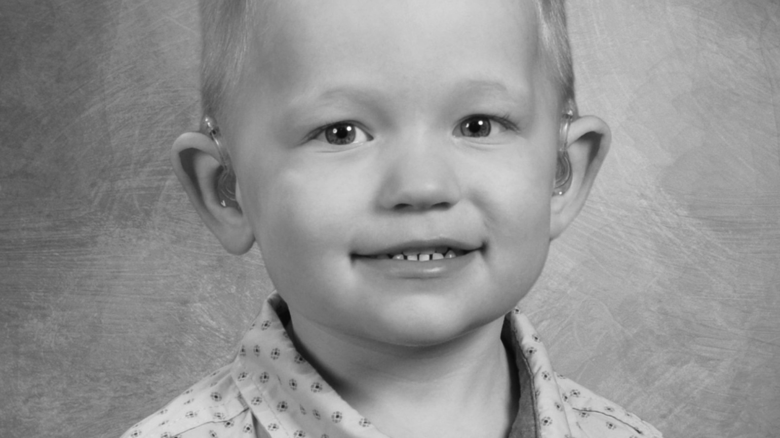 A young boy wearing a button-down shirt smiles at the camera for a school portrait.