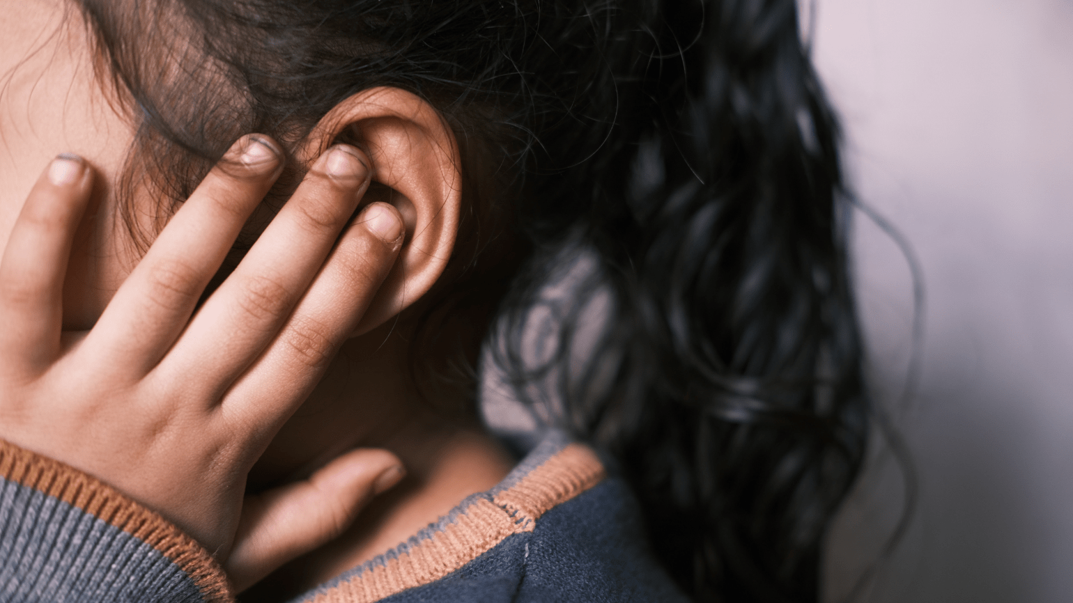 Side view of a young girl holding a hand up to partly cover her ear.