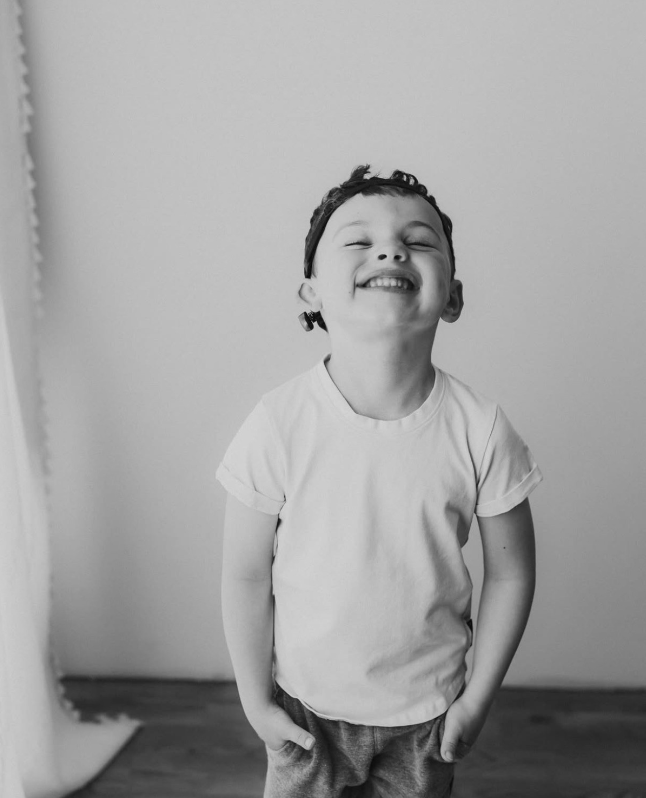 Henry, a young boy wearing a white shirt and backward baseball cap, smiles at the camera.