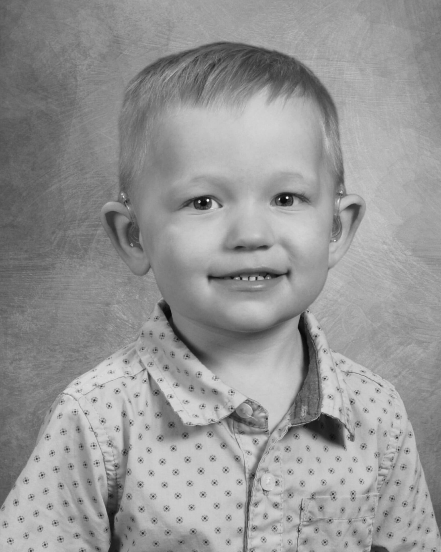 A young boy wearing a button-down shirt smiles at the camera for a school photo.