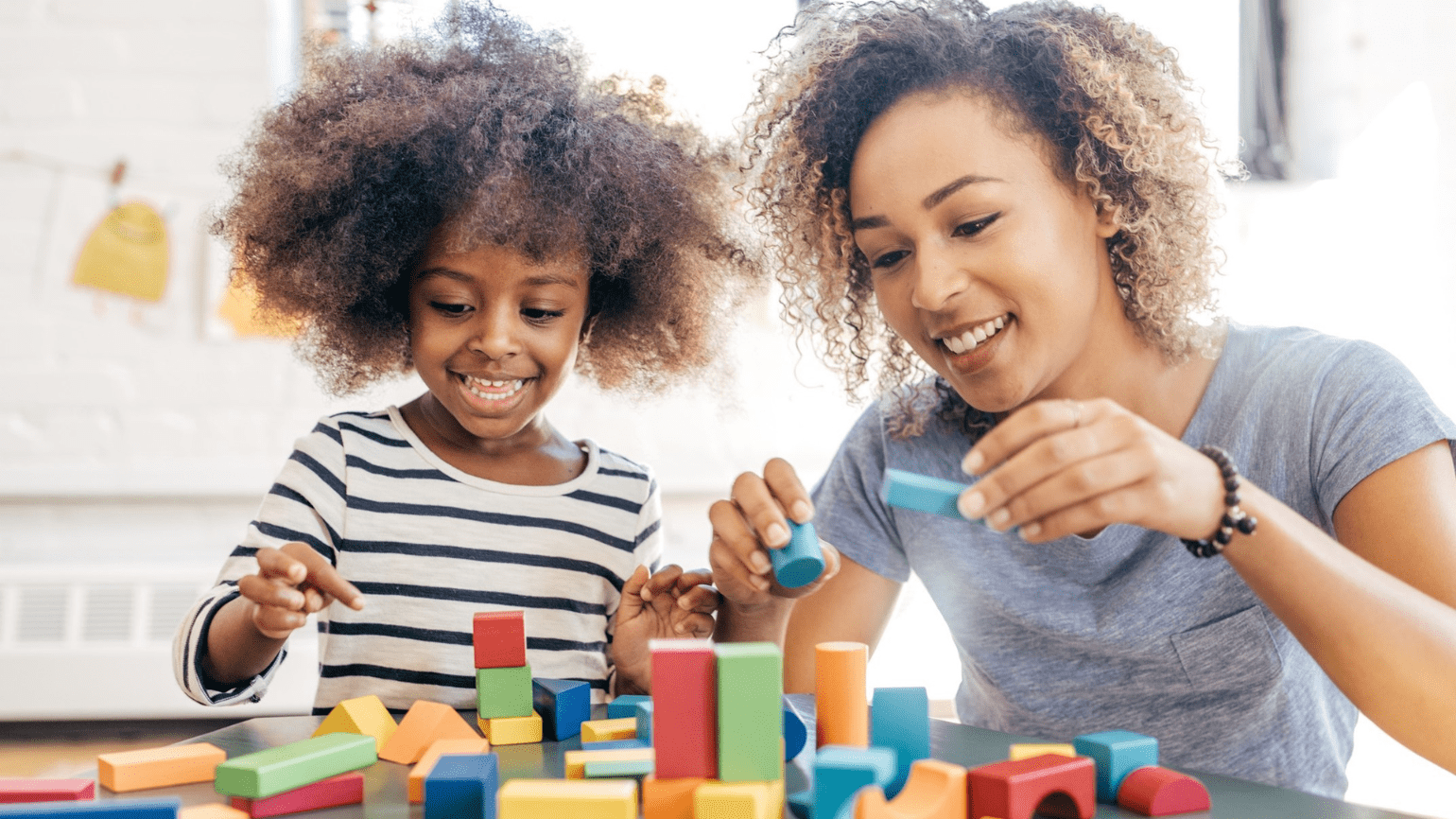 A woman and young child smile while playing with blocks.