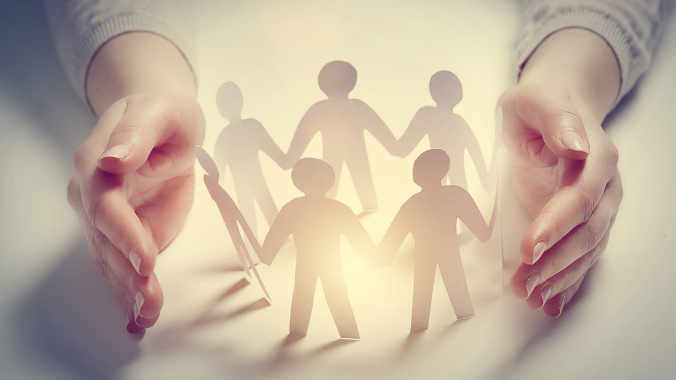 Two hands cupped around a paper cutout of people holding hands in a circle.