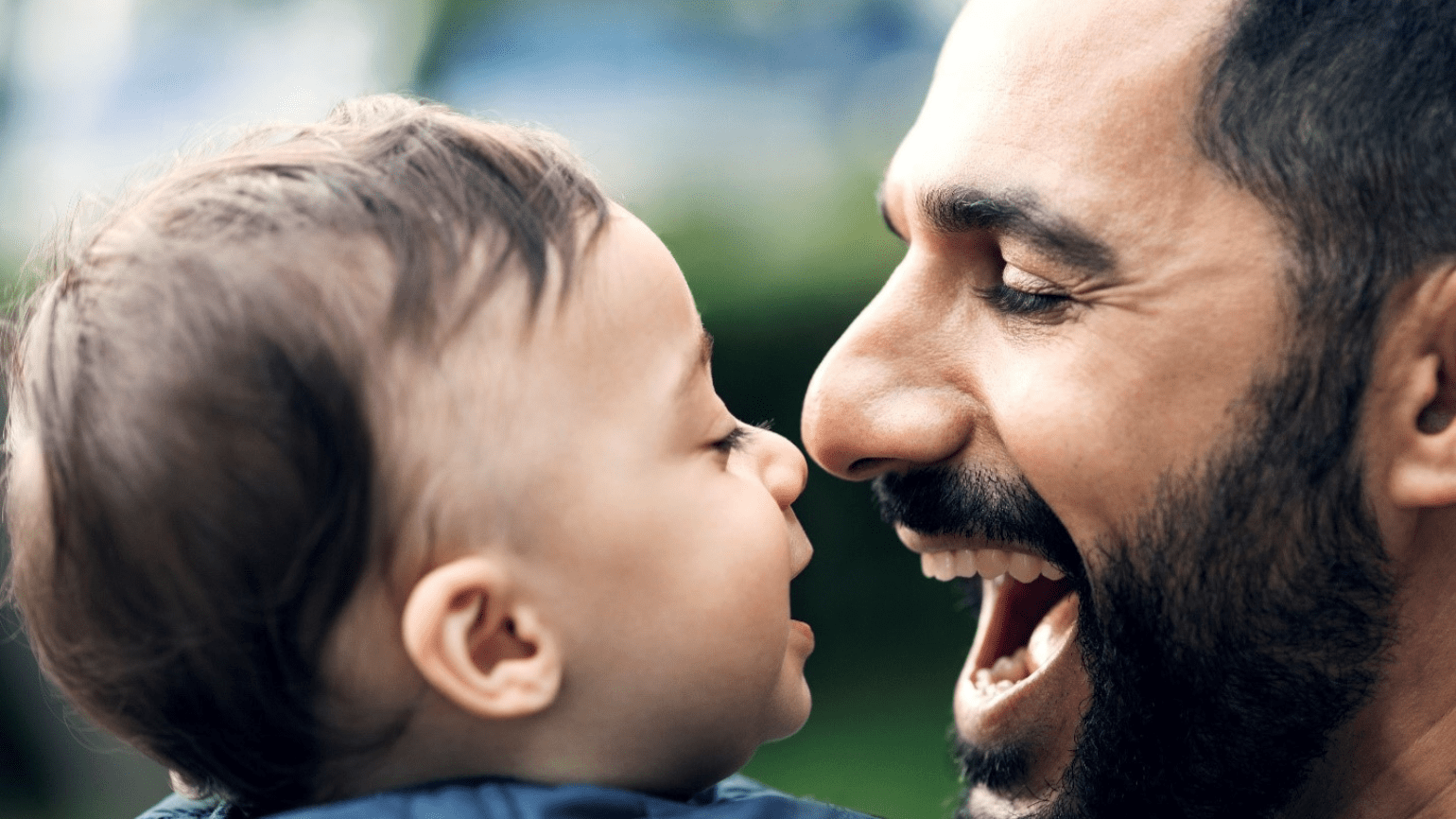 A dad smiles while nearly touching noses with his baby.