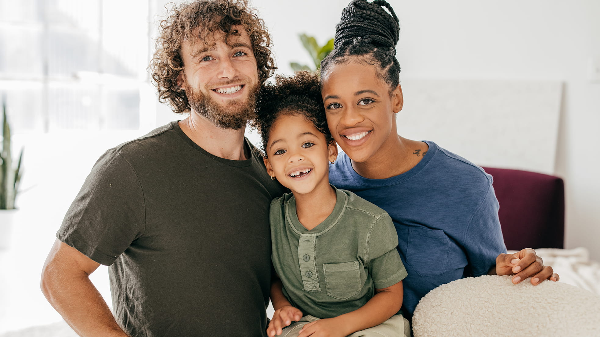 A mother, father, and young daughter smile at the camera.