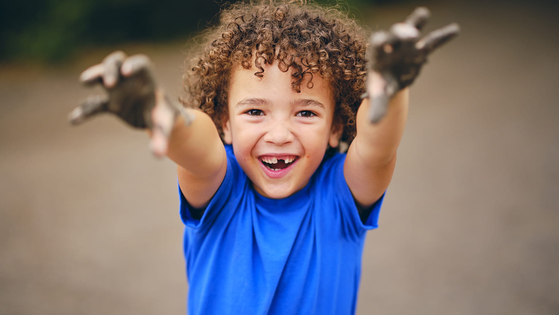 A happy little boy with mud covered hands smiling at the camera.