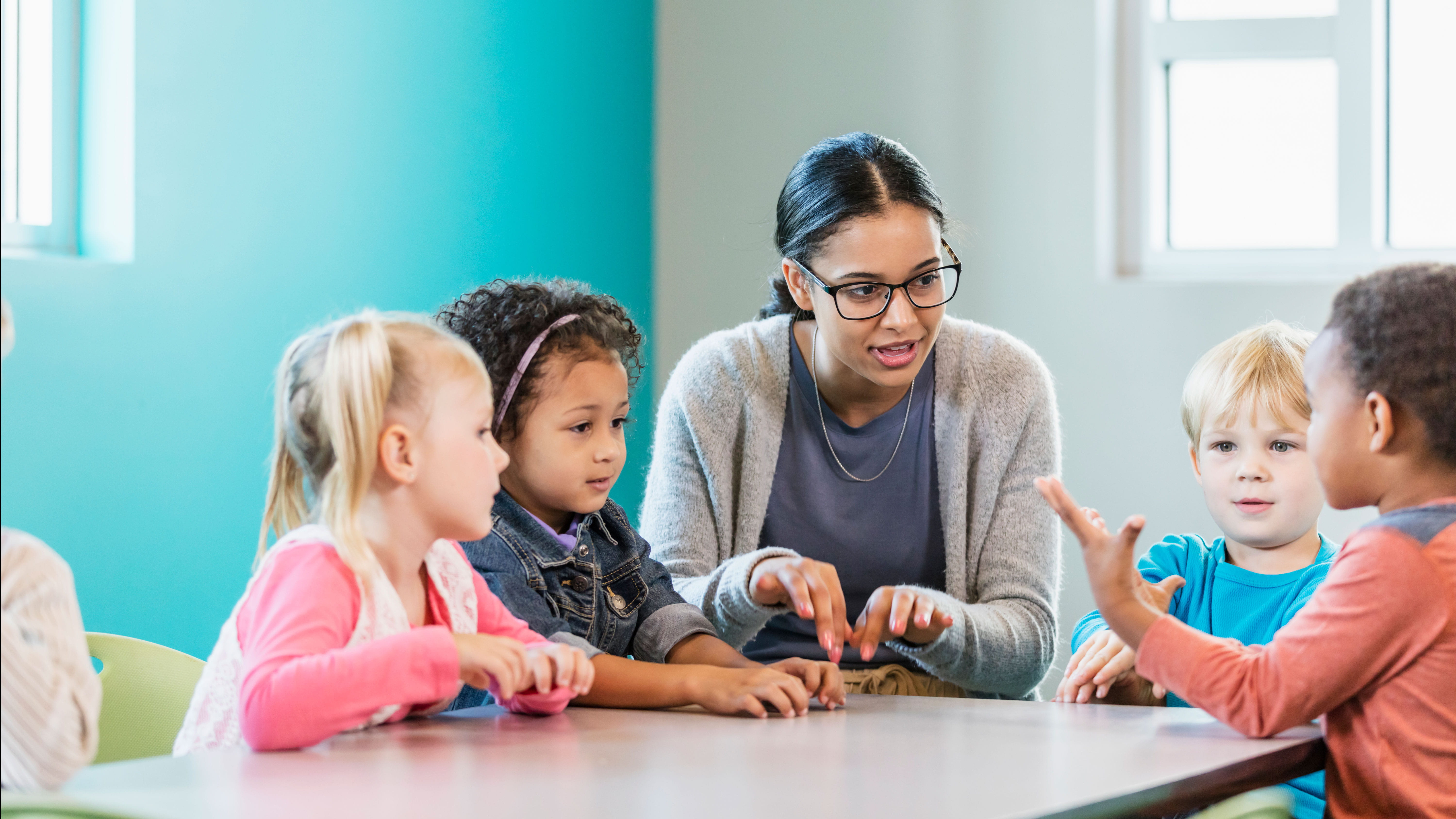 A teacher talks with four children seated at a table.