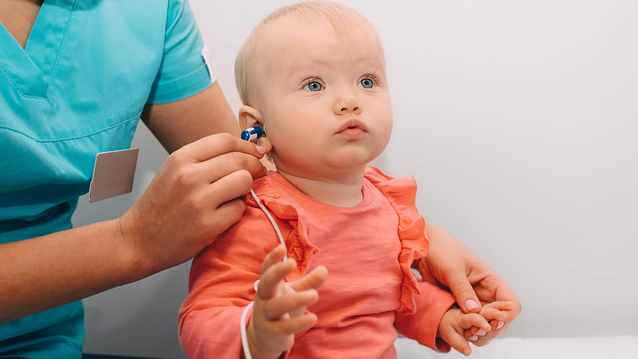 An adult places a hearing device in a baby's ear.