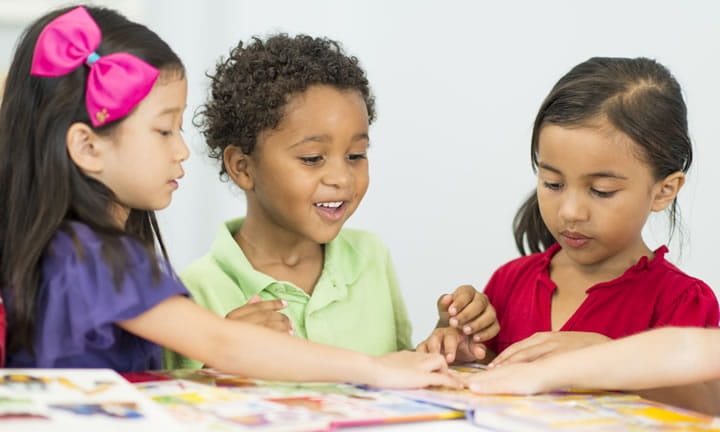 Three preschool children at a table looking at picture books together