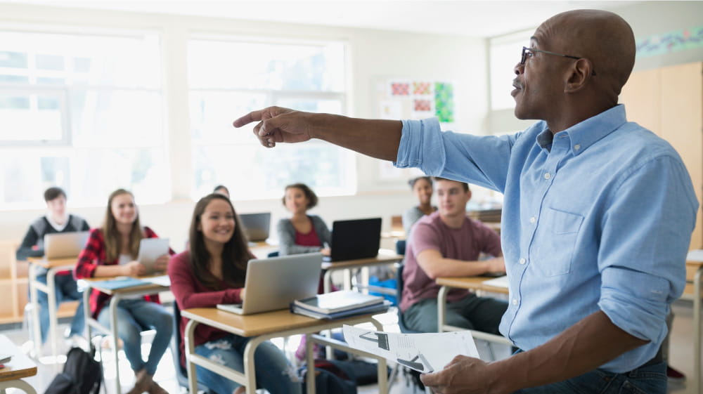 African American male teacher leading discussion of diverse students in a high school classroom.