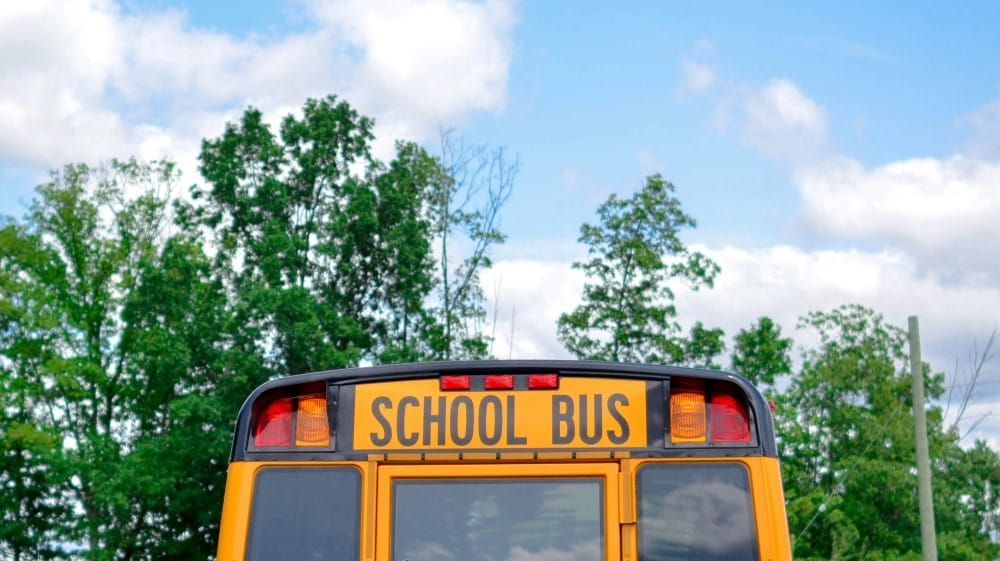 Top of the back of a school bus with trees and clouds in the background