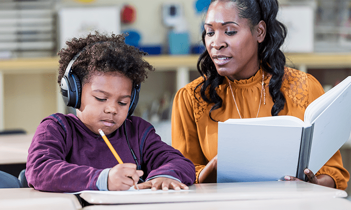 Young student with noise cancelling headphones working with a teacher.