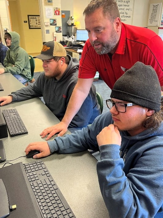 male educator assisting two male students at computers
